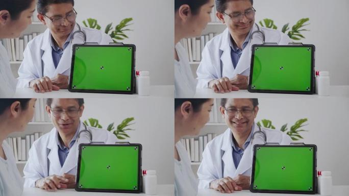 高级医生向患者解释在诊所办公室使用绿屏数字平板电脑并微笑。