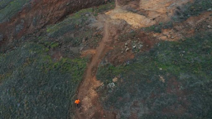 年轻的男性跑步者穿着防水夹克，在葡萄牙圣洛伦科岬角马德拉岛的岩石红橙绿色景观下奔跑。活跃的人概念4k