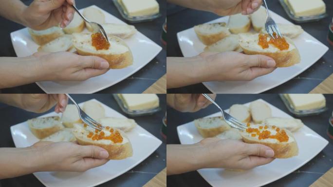 厨师在小点心上撒上红色鱼子酱。手在黄油面包上得到红色鱼子酱。用鱼子制作三明治的过程。家庭烹饪。美味开