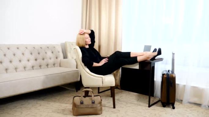 成功和成就概念。年轻成功的女人坐在扶手椅上，双腿放在昂贵的酒店公寓的桌子上。4k拍摄