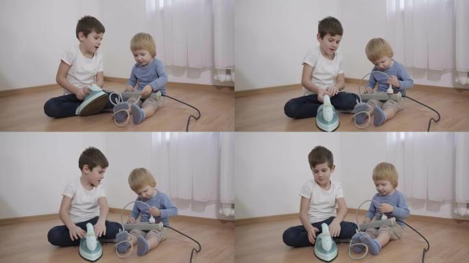 好奇的孩子在玩危险物品，小兄弟在房间里坐在地板上研究电熨斗和插座