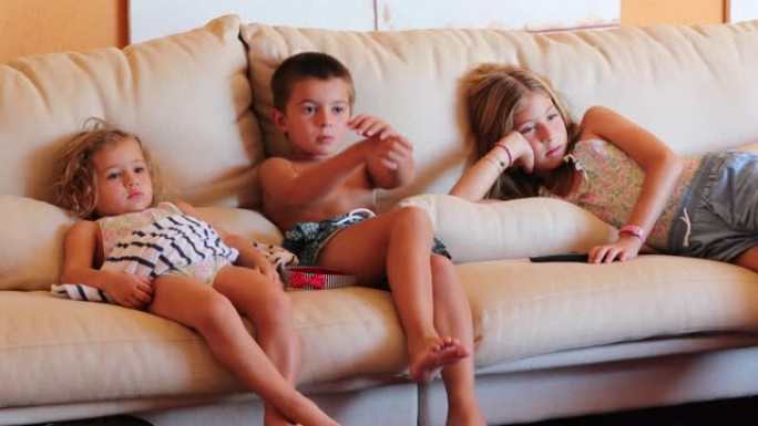 家里的孩子坐在客厅沙发上，孩子们盯着电视屏幕看电影