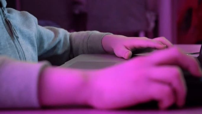 男孩点击鼠标并在键盘上打字。玩电子游戏和使用电脑的孩子。未来的rgb背光