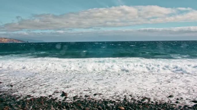 海上冲浪。海洋海岸，碧绿的海水和白色泡沫上的波浪。水滴飞入相机，火山黑岸的石头和沙子