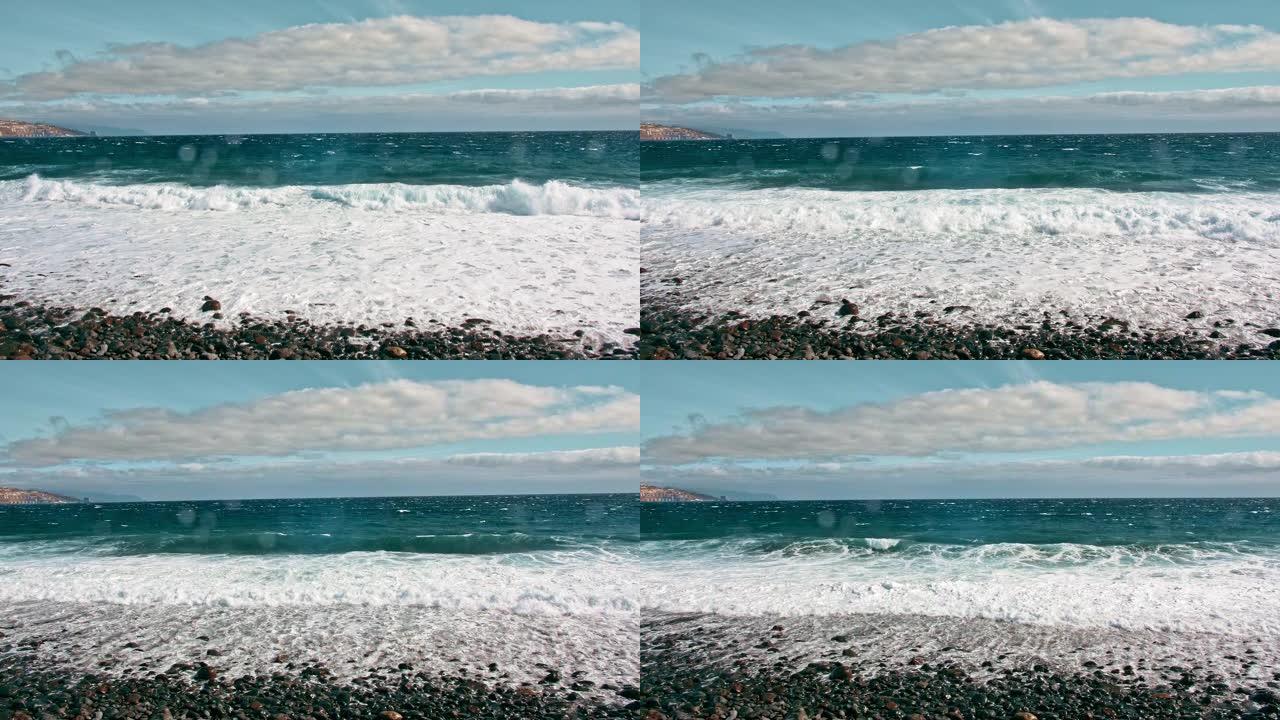 海上冲浪。海洋海岸，碧绿的海水和白色泡沫上的波浪。水滴飞入相机，火山黑岸的石头和沙子