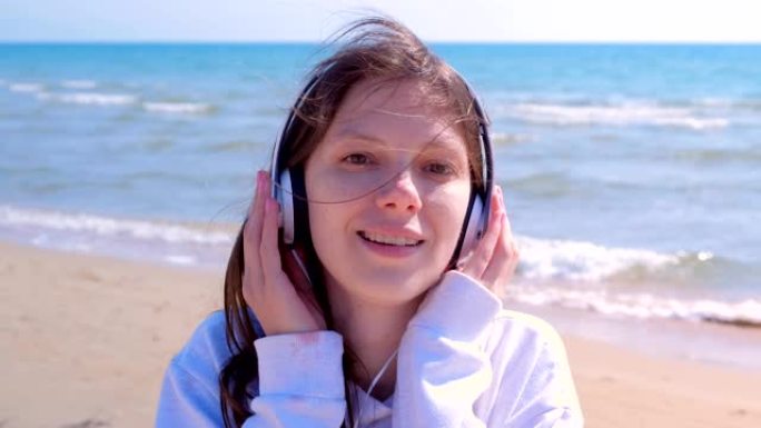 戴着耳机的年轻女子的肖像在沙滩上享受音乐漫步。