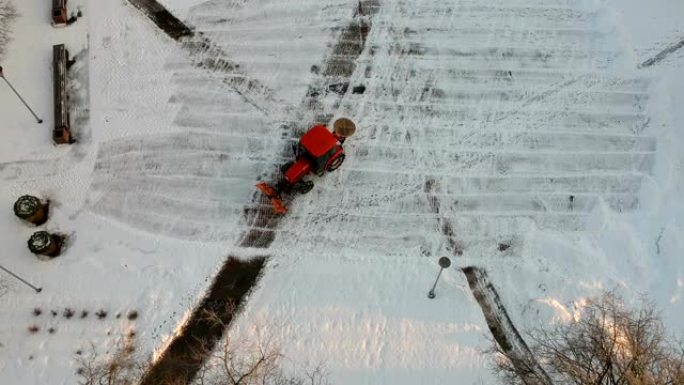 红色拖拉机清洁清除城市广场的新鲜积雪，空中