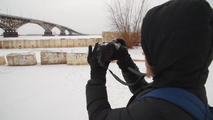 一个女孩在河边拍摄冬天的风景。女摄影师在城市的桥上拍照。