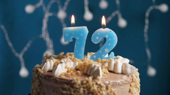 蓝色背景上有72号蜡烛的生日蛋糕。蜡烛着火了。慢动作和特写视图