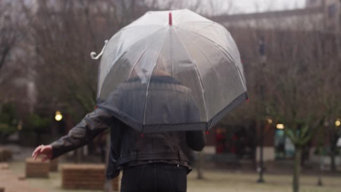 一名妇女手持透明圆顶伞在城市的雨天从一个步骤跳到另一个步骤