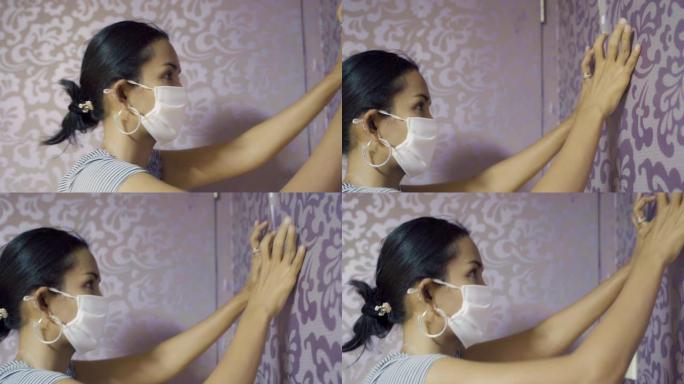 年轻的亚洲女性试图用自己和面罩保护来粘合和固定壁纸。做家务概念。