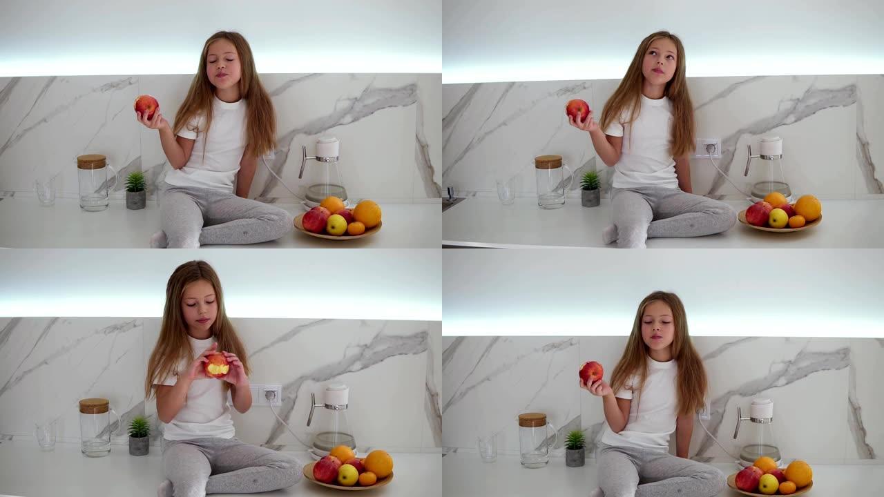 留着长发的小女孩坐在柜台上，在明亮的现代厨房里吃红苹果。她旁边有一碗新鲜水果。享受新鲜苹果的女孩