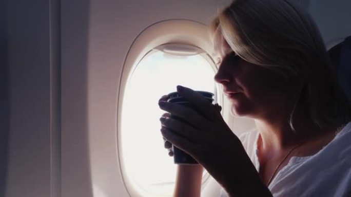 一个女人在飞机机舱里喝咖啡。坐在窗边