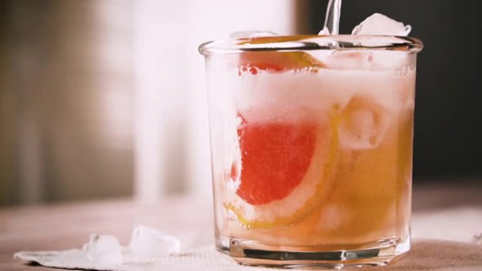 酒保正在准备一杯含有葡萄柚和冰的鸡尾酒，慢动作。葡萄柚鸡尾酒，特写。