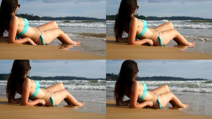 穿着比基尼的漂亮女孩躺在海岸上，晴天放松。年轻女子在海边晒日光浴，欣赏美丽的海景。暑假或假期的概念。