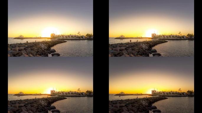 在石质海岸的日落时间流逝，渔民所在的地方是用船在地平线上捕鱼，阳光照射在大加那利岛的城市建筑后面。