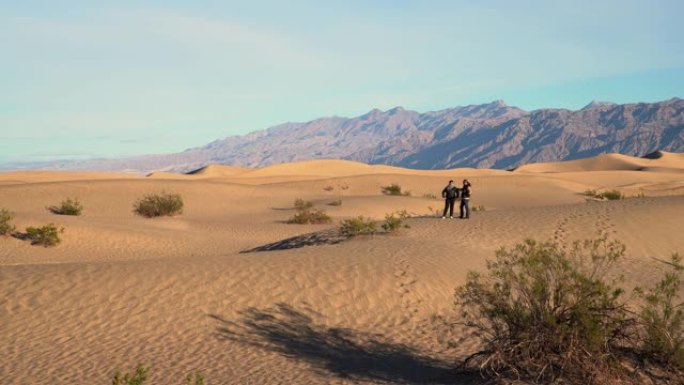 男人和女人在加利福尼亚州死亡谷的梅斯基尔公寓的沙丘上徒步旅行。