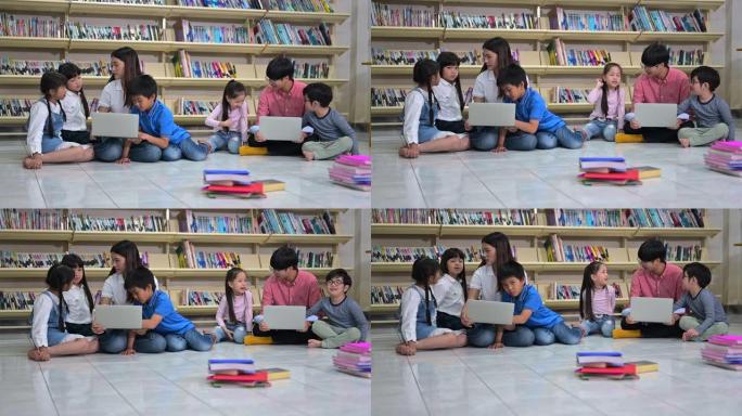 一群亚洲小孩从老师那里学习使用笔记本电脑，坐在学校图书馆的地板上，背景是书架