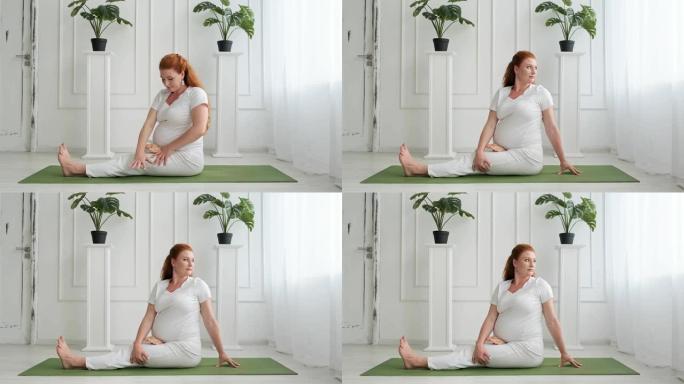 美丽的红发女人怀孕在家做地板瑜伽。母亲练习瑜伽
