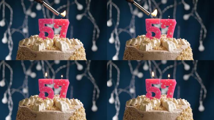 蓝色背景上有57号粉色蜡烛的生日蛋糕。蜡烛着火了。慢动作和特写视图
