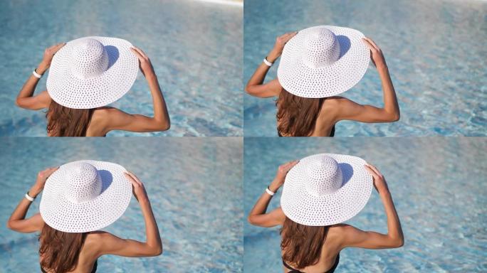 特写。模糊的水背景。一个戴着大白帽子的年轻女子坐在游泳池附近，戴着帽子。有文字的地方。ProRes 