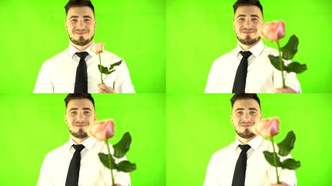 穿着白衬衫和领带的英俊男子微笑着在绿屏背景上呈现一朵玫瑰。有花的绅士