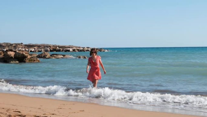年轻迷人的女孩沿着沙滩散步。黑发女孩在海边玩得开心。女孩在海边晒太阳。女孩在海水附近的海滩上放松。女