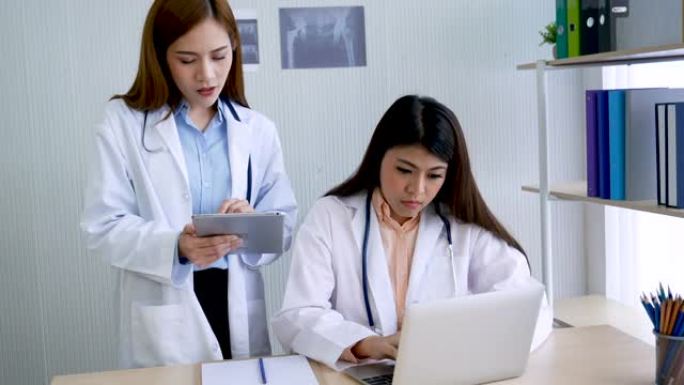 两名女医生在医院医疗保险治疗诊所咨询专业专家诊断。医生使用笔记本电脑为医疗保健肿瘤学家治疗开处方。