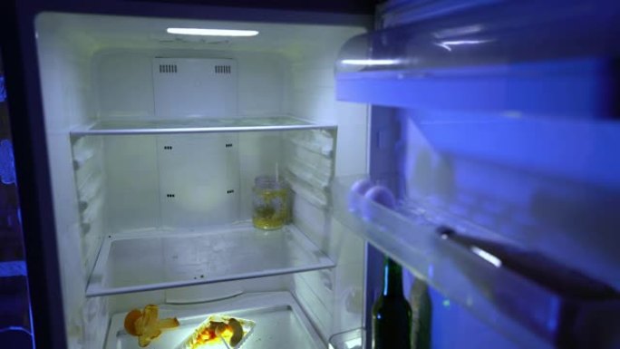 在冰箱里找食物的人。一名男子将啤酒和未食用的罐头放入冰箱。