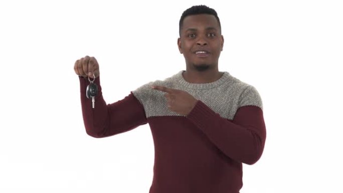 英俊快乐的非洲裔美国男子拿着车钥匙，指着它，孤立在白色背景上