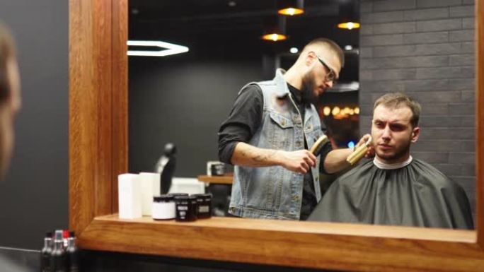 在理发店里，戴眼镜的理发师用剪子剪了胡子男人的头发。沙龙中的潮人发型设计和理发。用修剪器梳理头发。理