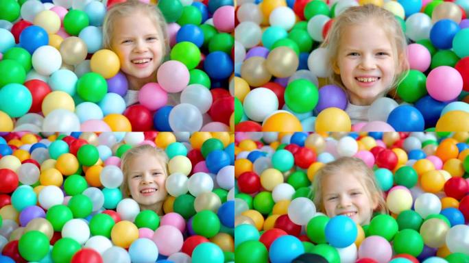 可爱的金发小女孩躺在游戏中心大干戏水池里的多色塑料球上。对着镜头微笑。肖像特写。在游戏室玩得开心。休