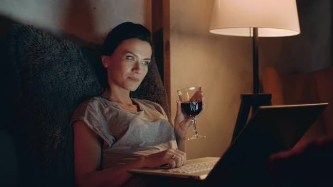 女孩在沙发上的笔记本上上网。用笔记本电脑喝红酒的女人。