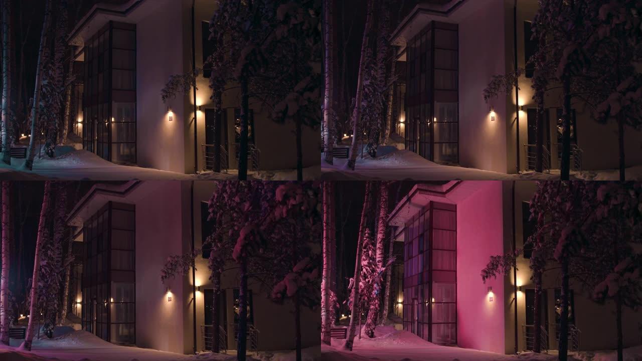 冬末傍晚的大房子的外墙被一辆急救车的五颜六色的闪光灯照亮。库存镜头。晚上下雪冬天的小屋的户外景色