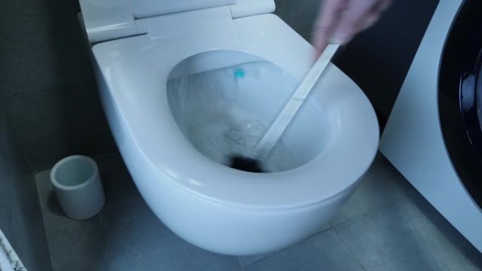 男手正在用刷子清洁白色马桶，特写镜头。男子在浴室用海绵洗白色马桶，墙壁和地板上有灰色瓷砖，侧视图
