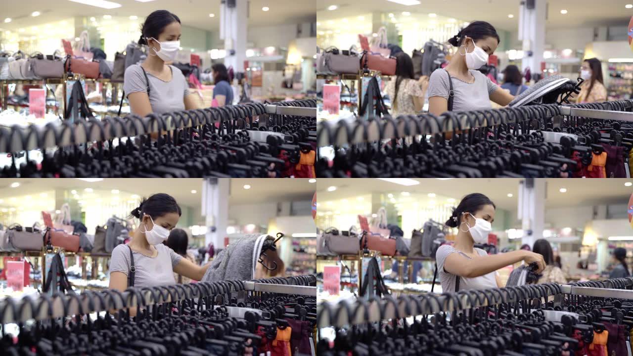 年轻的亚洲女性在带有面罩保护的购物中心中选择和购买衣服，包和配饰服装。