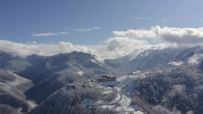 从着陆飞行无人机，在多云的天空景观上，雪峰上的山村。鸟瞰雪山度假村的蜿蜒道路。福吉天空上令人叹为观止