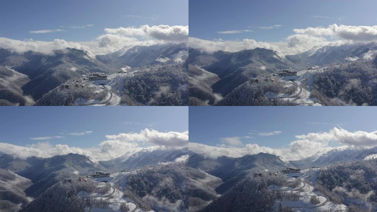 从着陆飞行无人机，在多云的天空景观上，雪峰上的山村。鸟瞰雪山度假村的蜿蜒道路。福吉天空上令人叹为观止