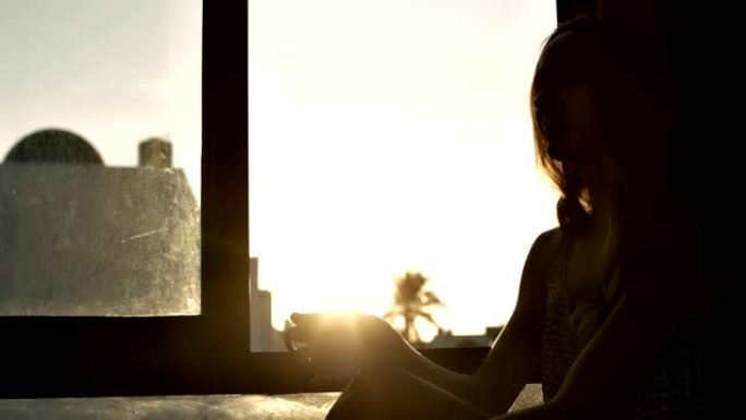 女孩剪影在明亮的窗户上喝咖啡