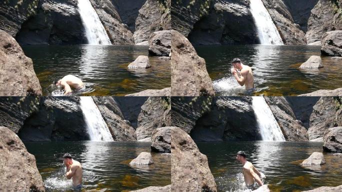 男性游客站在湖里洗脸。男士旅行者在自然游泳池休息，享受夏季旅行。汹涌的瀑布倾泻在热带雨林的垂直岩石悬