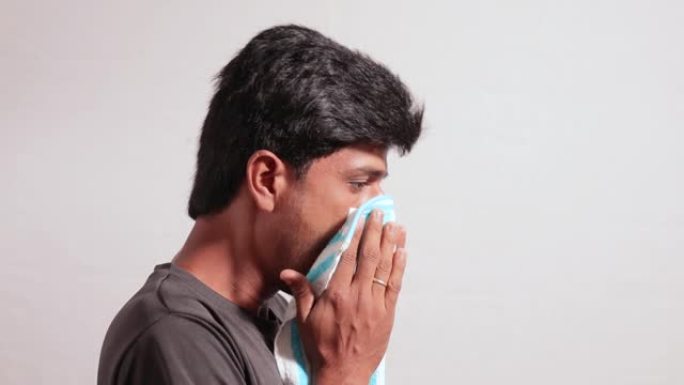 生病的健康年轻人打喷嚏或咳嗽通过在孤立的背景上覆盖他的脸和鼻子-概念显示冠状病毒或covid 19建