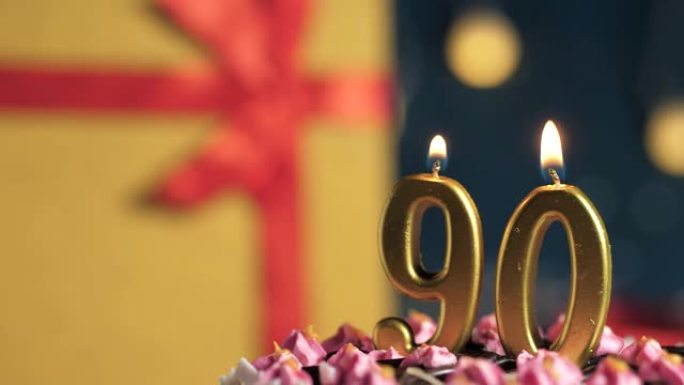 生日蛋糕90号点火器燃烧的金色蜡烛，蓝色背景礼物黄色盒子用红丝带绑起来。特写和慢动作
