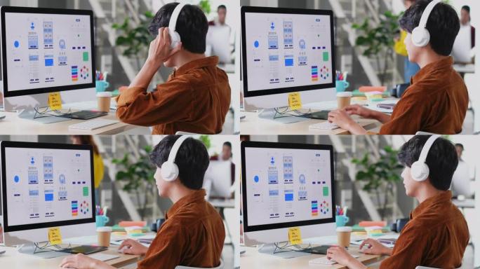 年轻的亚洲程序员男子戴着耳机在现代创意办公室的电脑桌面上编码移动应用程序，忙碌的亚洲ux，ui设计开