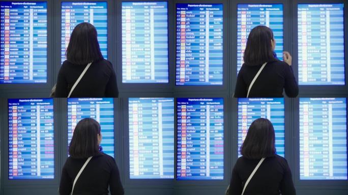 亚洲年轻旅游女子在机场看航班信息显示。