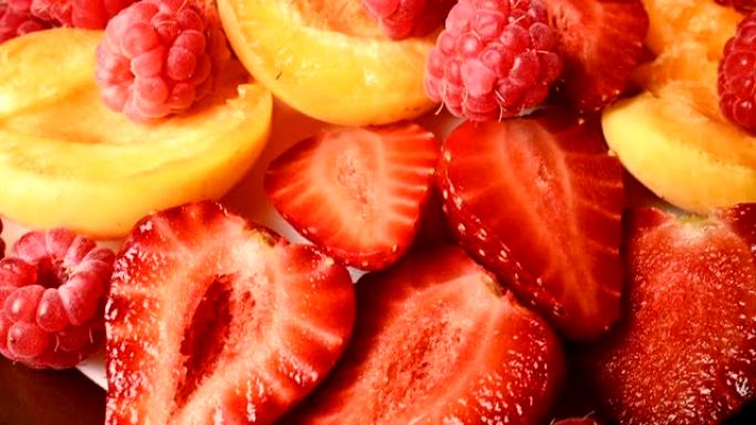 盘子上杏子旁边切成薄片的红色草莓和覆盆子的特写镜头。现场摄像机。美味有益健康的饮食和素食的概念。