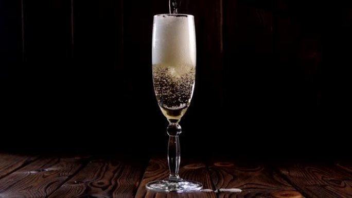 将香槟倒入木制背景上的玻璃杯中的特写镜头，慢动作。