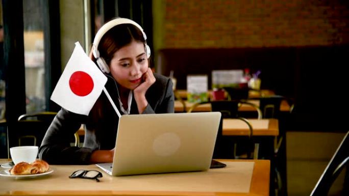 商业女性从笔记本电脑上观看在线体育，挥舞着日本国旗欢呼日本。