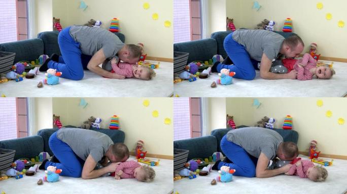 快乐的年轻父亲在家里玩具之间的地毯上挠蹒跚学步的女儿。