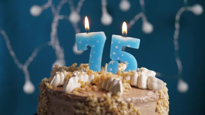 蓝色背景上有75号蜡烛的生日蛋糕。蜡烛吹灭了。慢动作和特写视图
