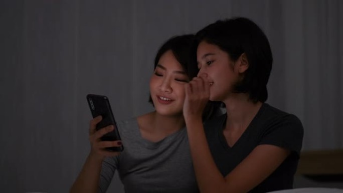 一对亚洲少女看手机，晚上在卧室里一起聊天